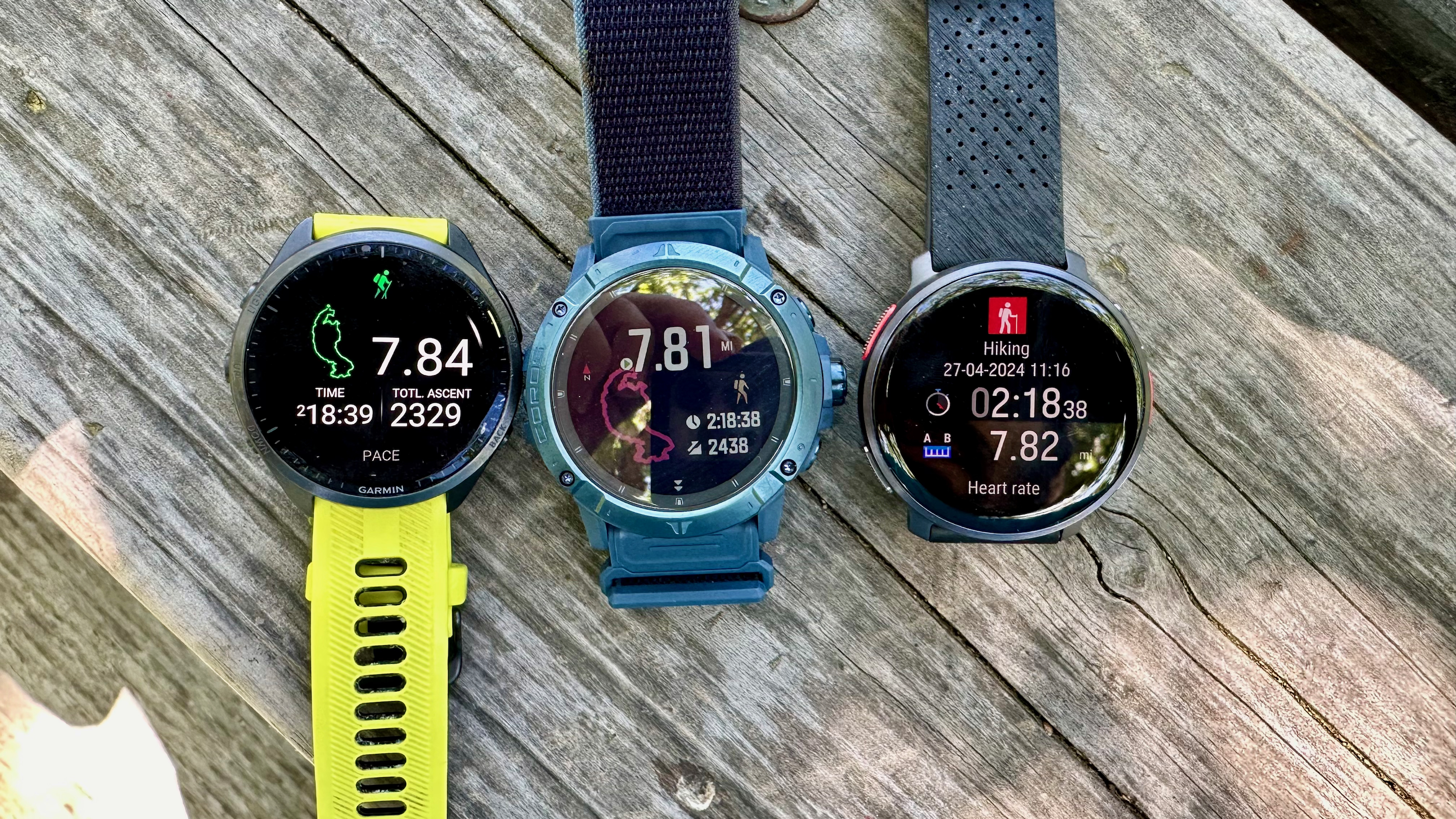 The Garmin Forerunner 965 (left), COROS VERTIX 2S (center), and Polar Vantage V3 (right) sitting on a table together, all showing post-hike result screens.
