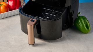 a large black 5.3 quart capacity air fryer with black touchscreen and rose gold embellishments sits upon a brown table with a blue background