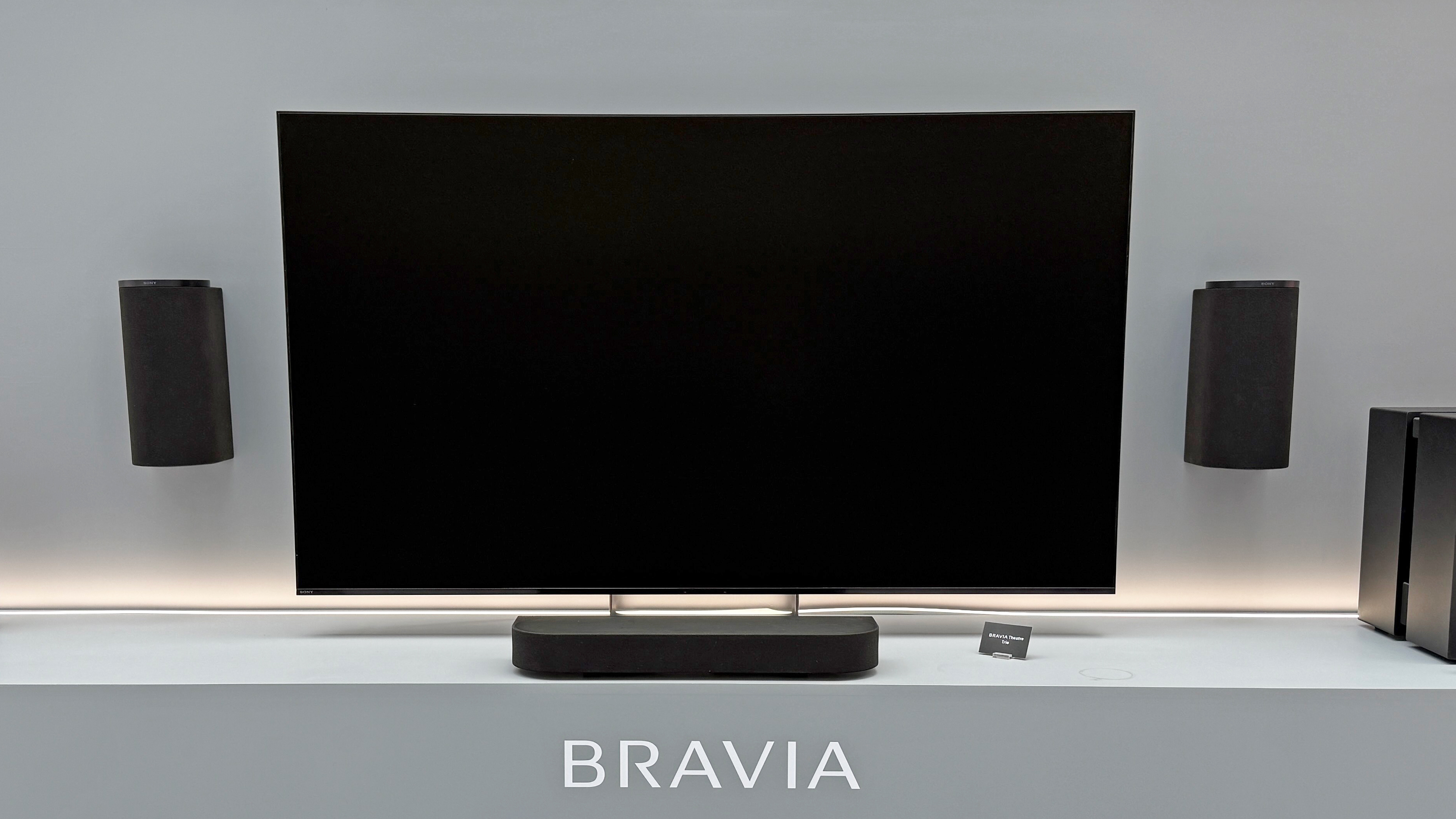 The Sony Bravia Theatre Trio with a black TV screen. Two speakers are hanging on the wall, either side of a TV with a small speaker underneath it