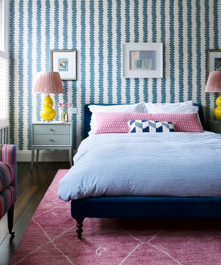 Bedroom with blue and white wallpaper, dark wood floor and pink rug, double bed and grey bedside tables.