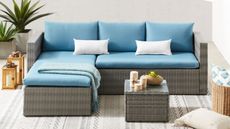 A rattan corner sofa with chaise lounger and blue cushions on a patio terrace