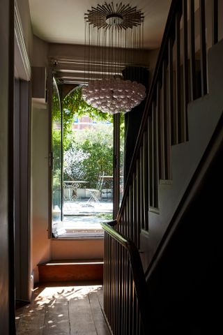 Wooden staircase, low hanging glass ball chandelier, large mirror reflecting into patio area