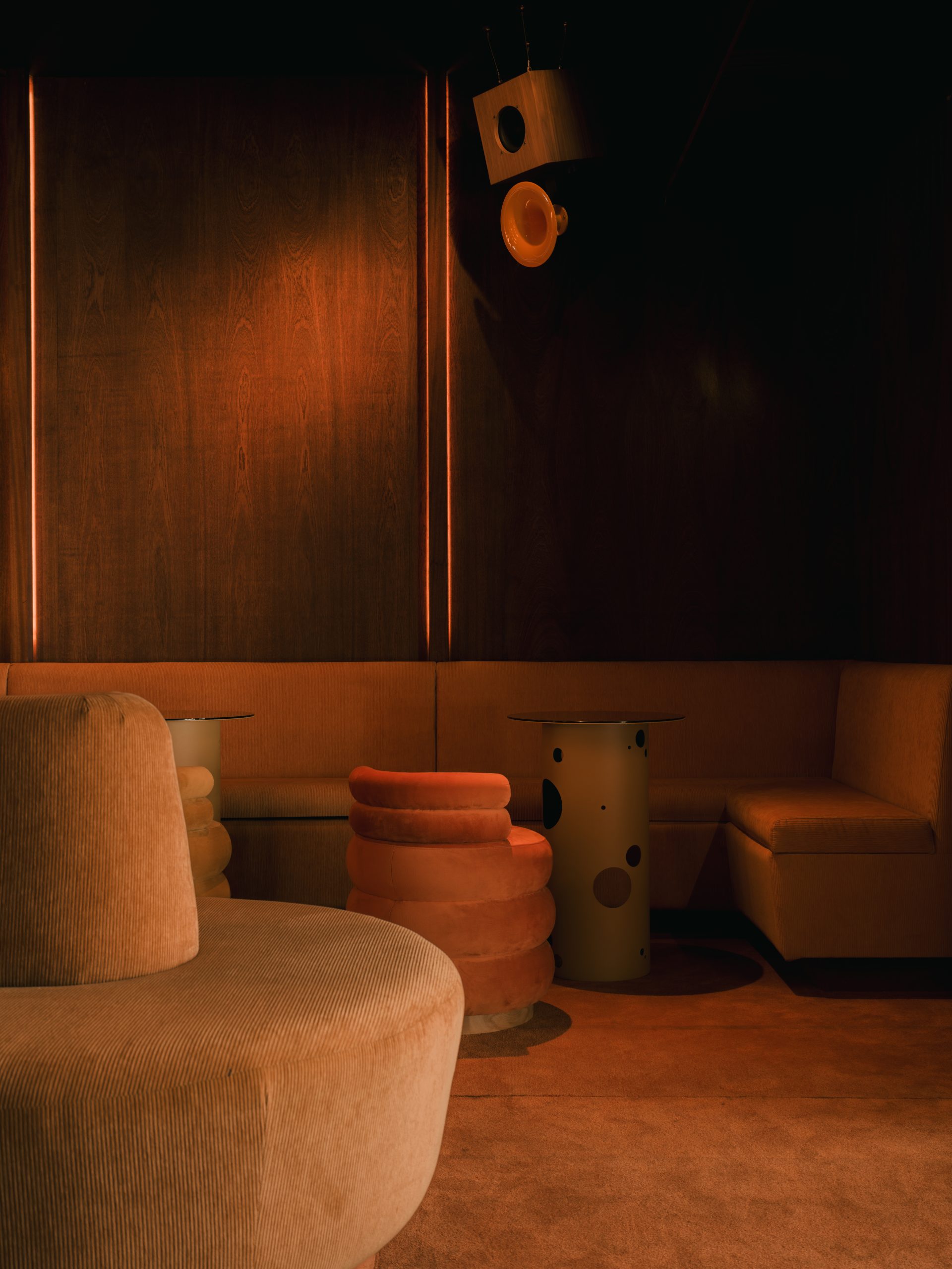 A dimly lit bar with red and orange-tinted interiors sculpted in wood, chrome, lacquer, velvet, and marble features sinuous banquettes, atmospheric sconces, geometrical skylights, and refined details.