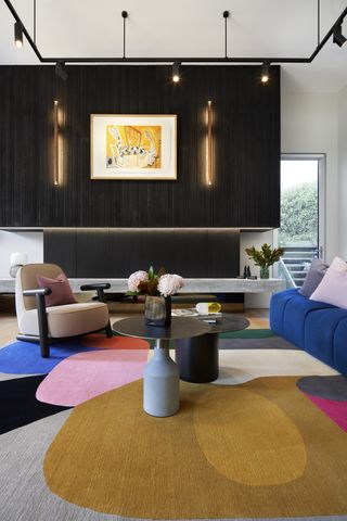 black painted walls in a living room with black stools and a carpet that has black, pink yellow and blue hues