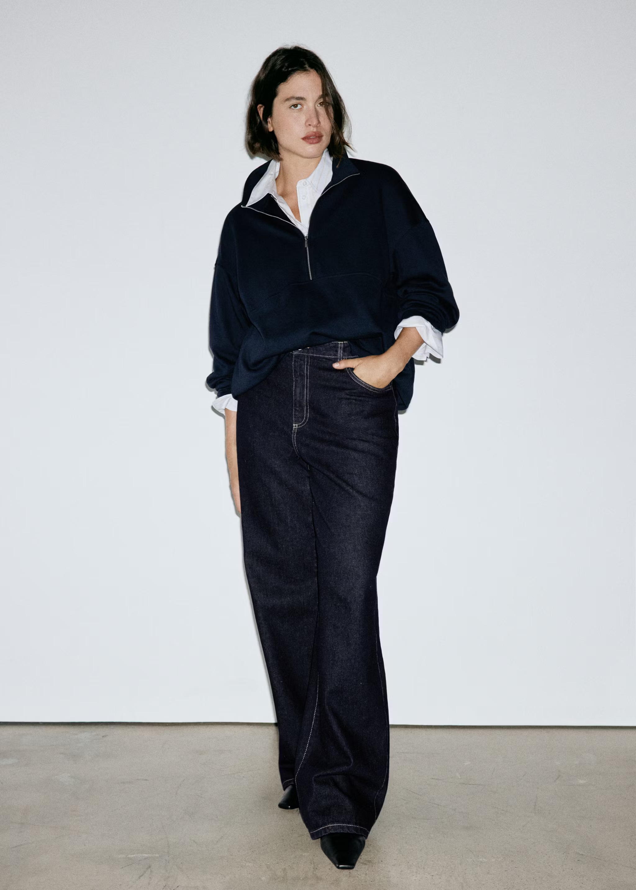 An image of a Mango model wearing dark indigo, wide-leg jeans with a navy half-zip and button-down shirt