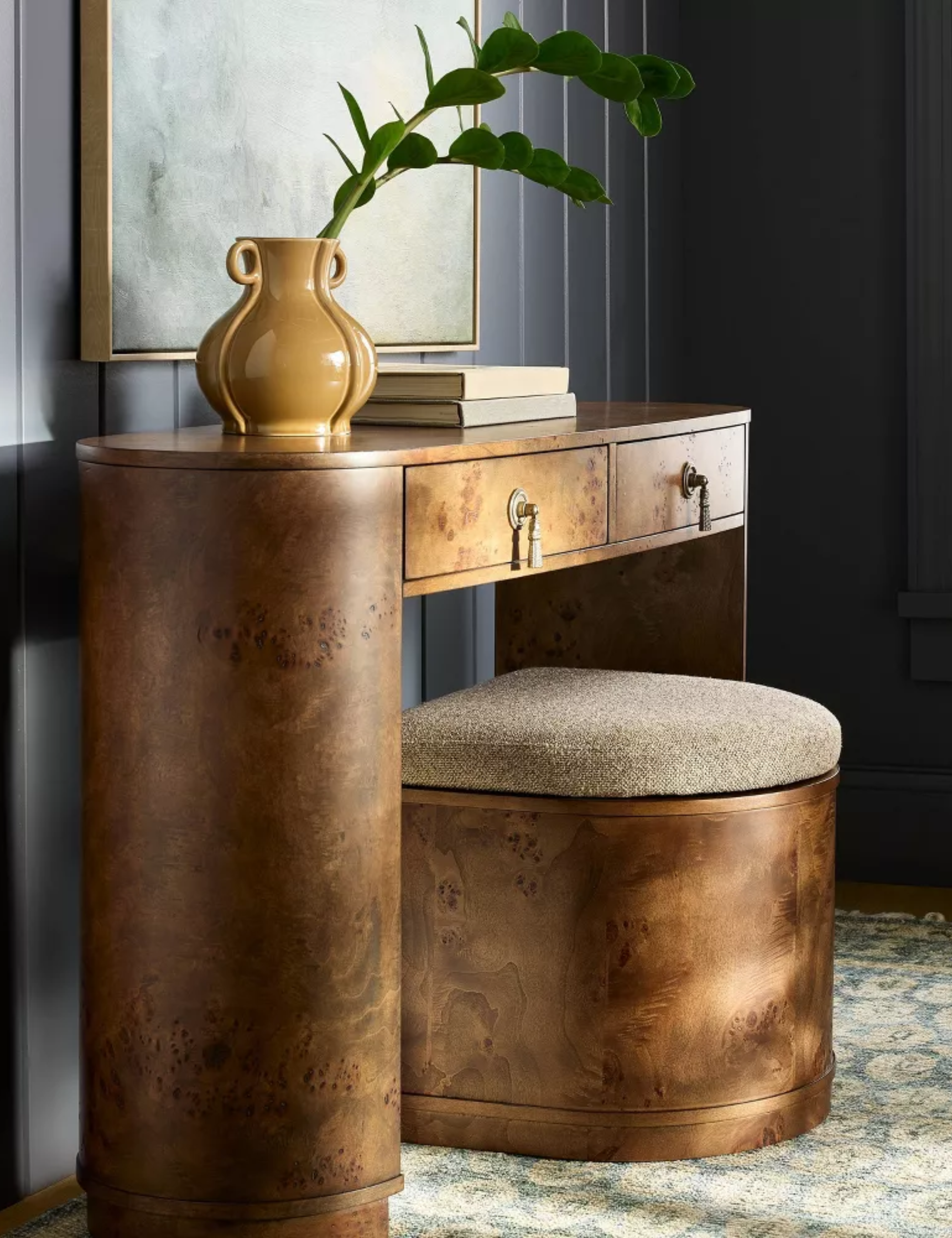 Shea McGee burled wood storage ottoman tucked under a coordinating burled wood desk inside of a navy wood paneled room with a large windowpane