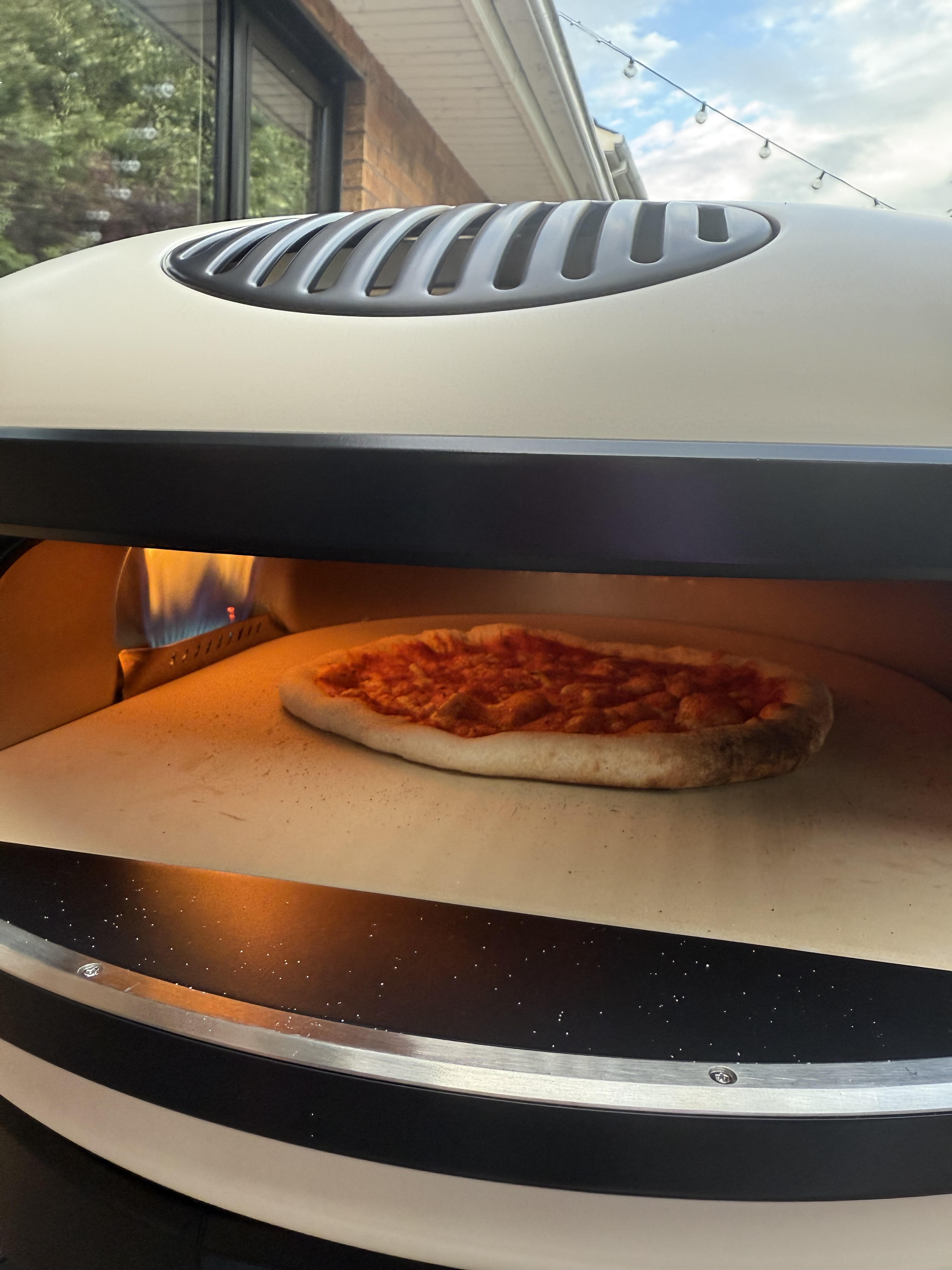 A Gozney XL Pizza Oven in bone white up close with a pizza cooking inside with the flame in view