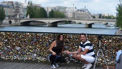 A couple pose with 'lovelocks' on a Parisian bridge