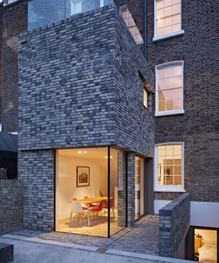 exterior shot of tall modern brick extension with corner glazing lit from inside