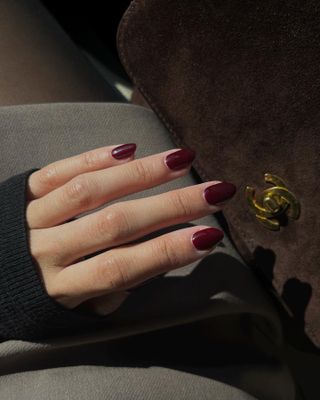 Dark red manicure next to brown Chanel handbag