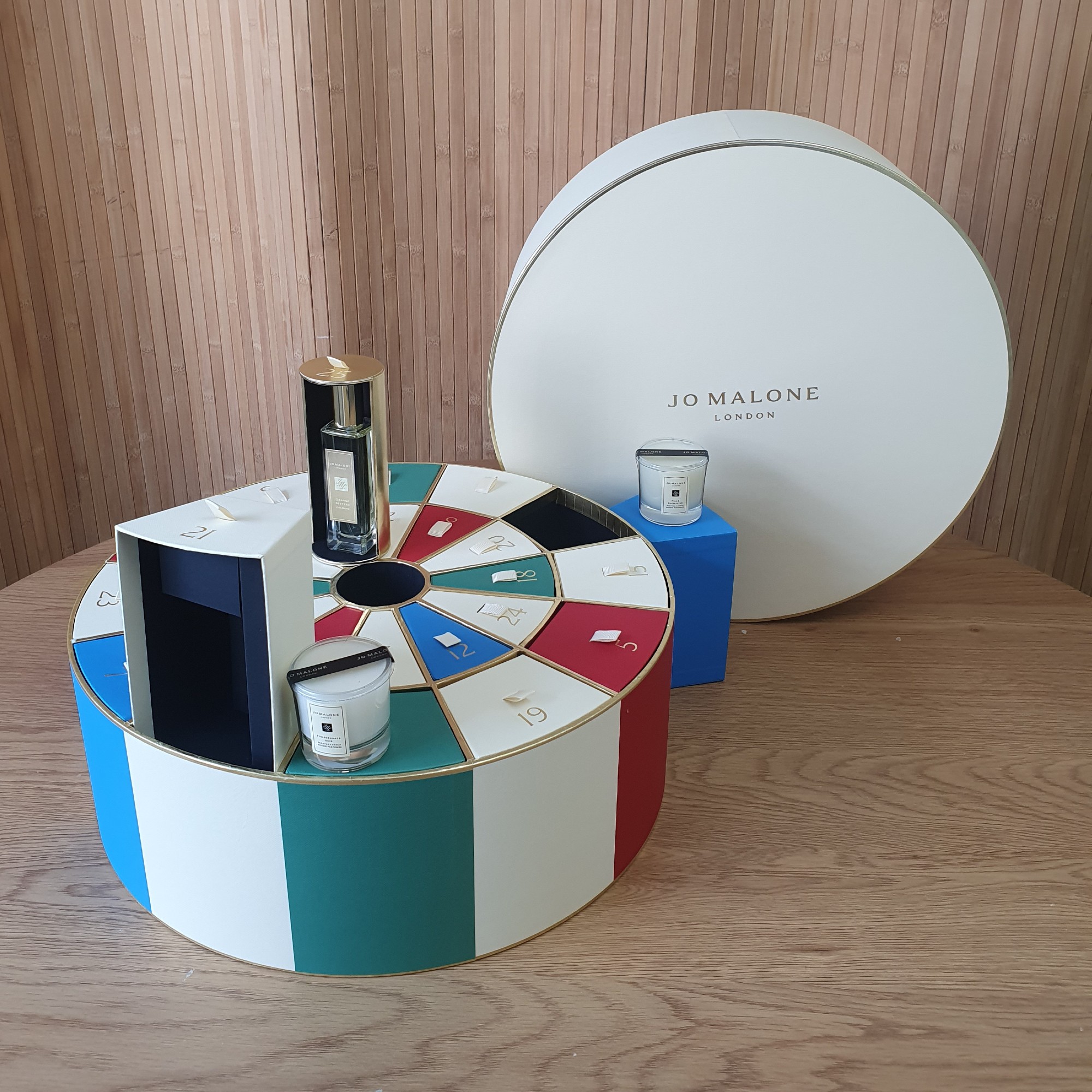 Jo Malone advent calendar with open compartments on a wooden table with a panelled backdrop