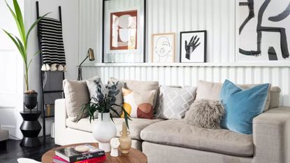 White modern paneled living room with grey couch, wooden coffee table, and artwork leaning on the char rail