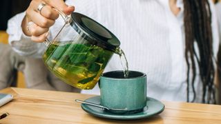 A woman pours a green tea into a turquoise cup