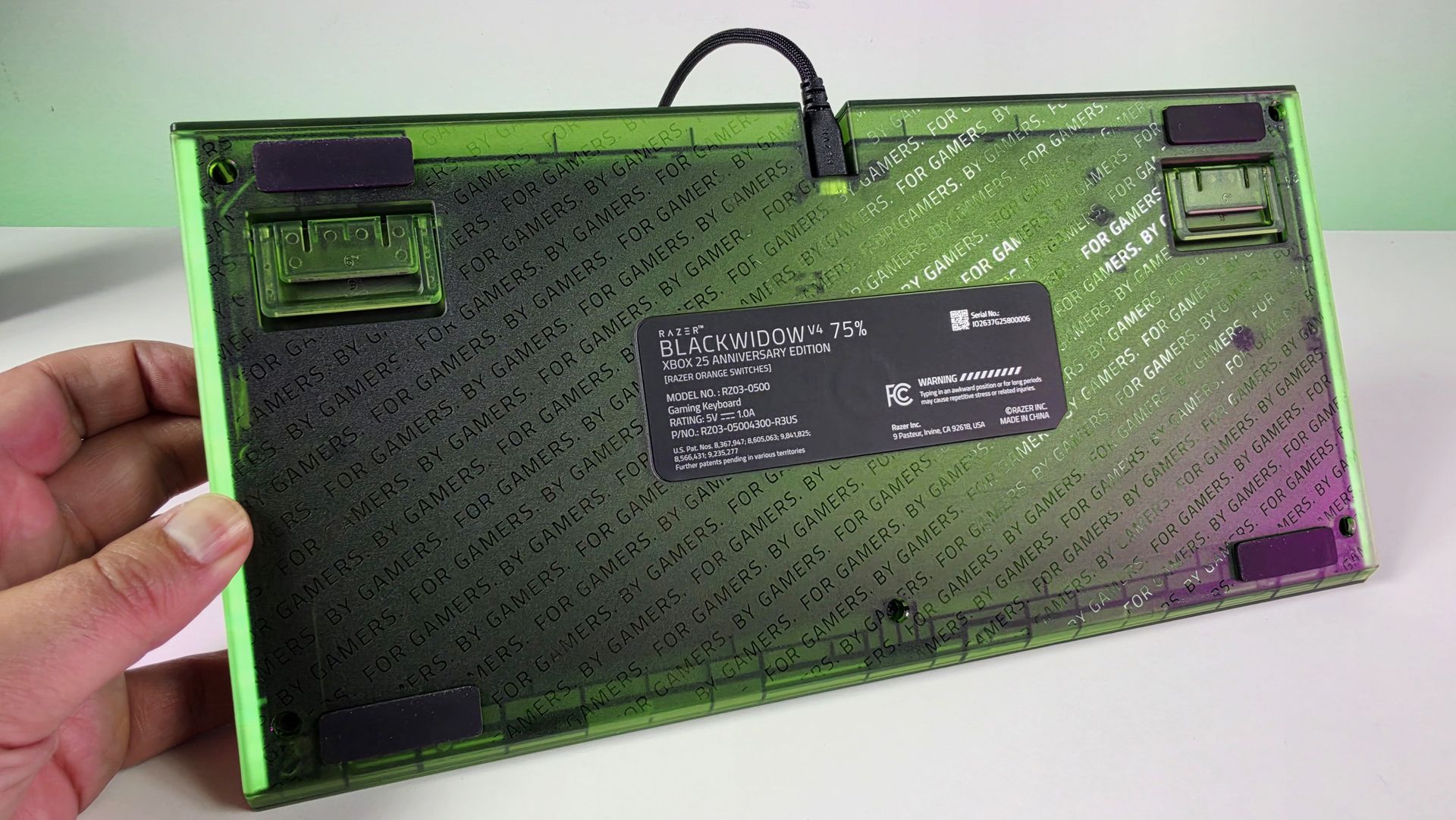 Underside of the Razer BlackWidow V4 75% keyboard showing translucent green casing with repeating 'FOR GAMERS. BY GAMERS.' text and specs label.