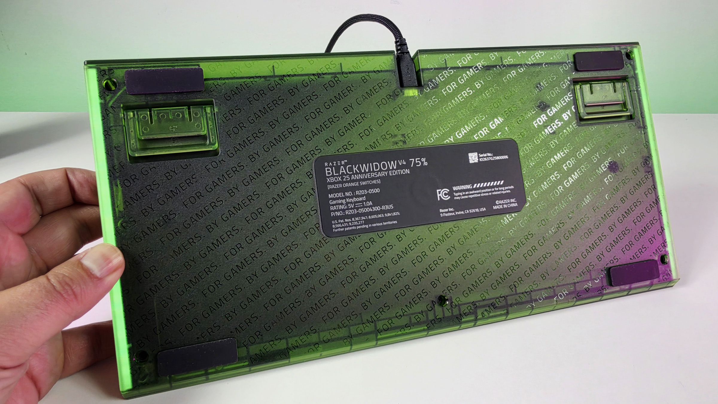 Underside of the Razer BlackWidow V4 75% keyboard showing translucent green casing with repeating 'FOR GAMERS. BY GAMERS.' text and specs label.