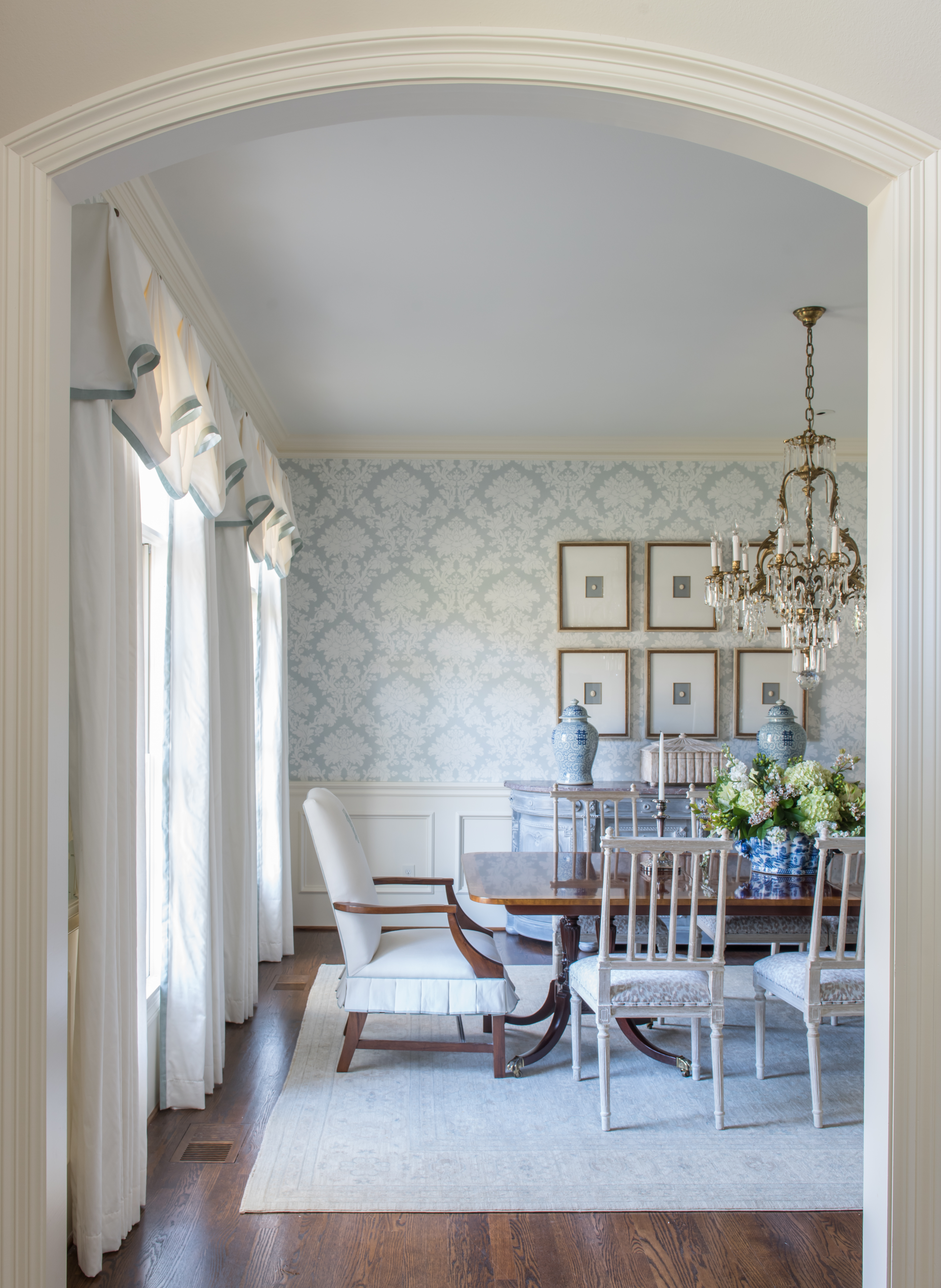 blue damask wallpaper in classic dining room with blue and white curtains, gold chandelier, mahogany table, upholstered dining chair, mahogany floor