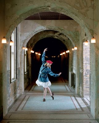 Woman wearing a blue jacket, white skirt and red hat, posing in an arched corridor