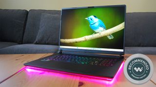 ASUS ROG Strix SCAR 18 gaming laptop on a wooden table with pink RGB underglow and a "Recommended" award badge from Windows Central