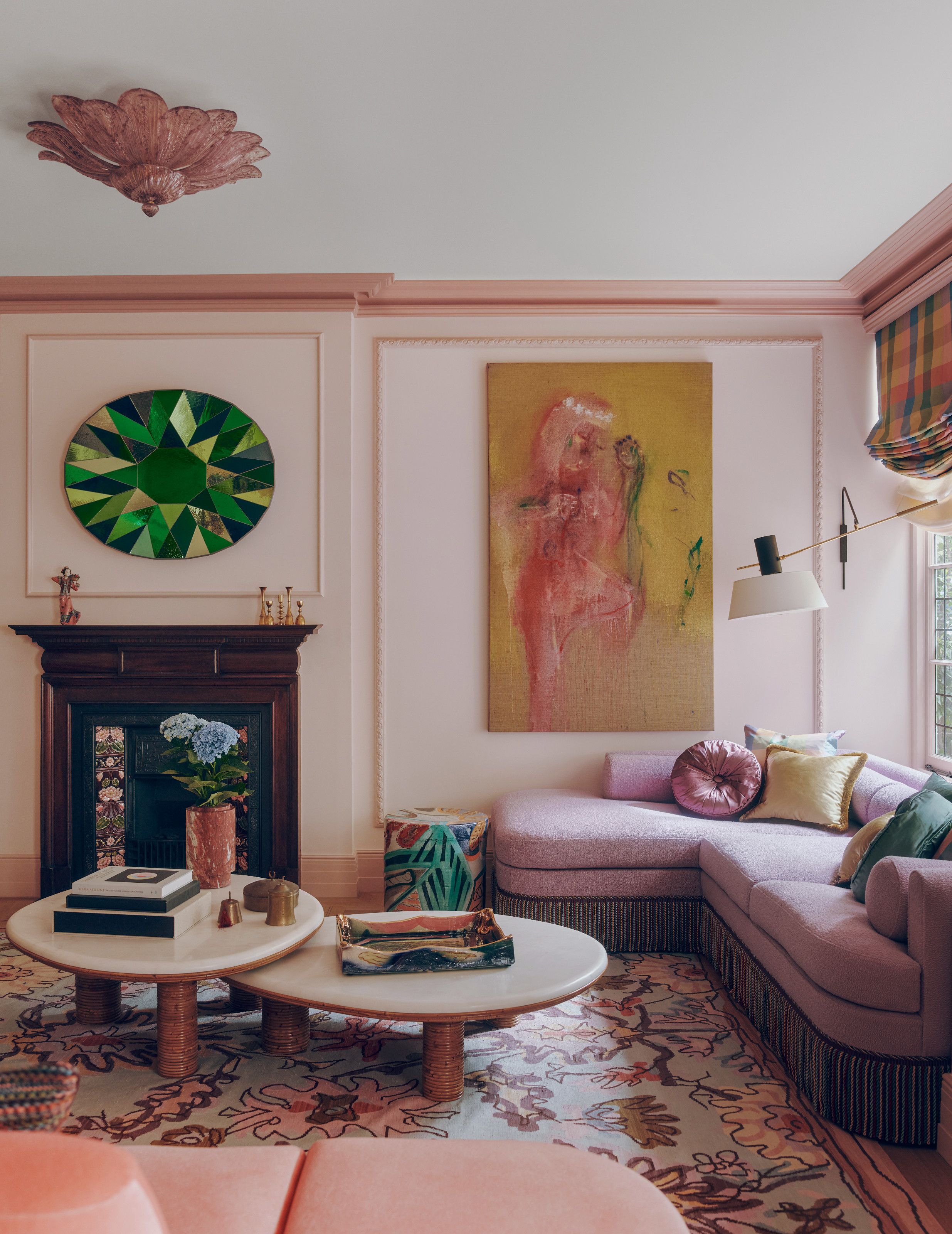 Pale pink living room with lilac corner sofa, two nesting coffee tables, floral rug, abstract artwork and green stained glass artwork