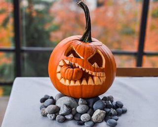 A pumpkin carving idea depicting a larger pumpkin 'biting' into miniature pumpkin with grey stones in foreground
