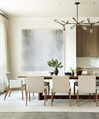 Dining room with wood floor and ivory area rug, white walls, ivory upholstered dining chairs, dining table, pendant light and large abstract artwork