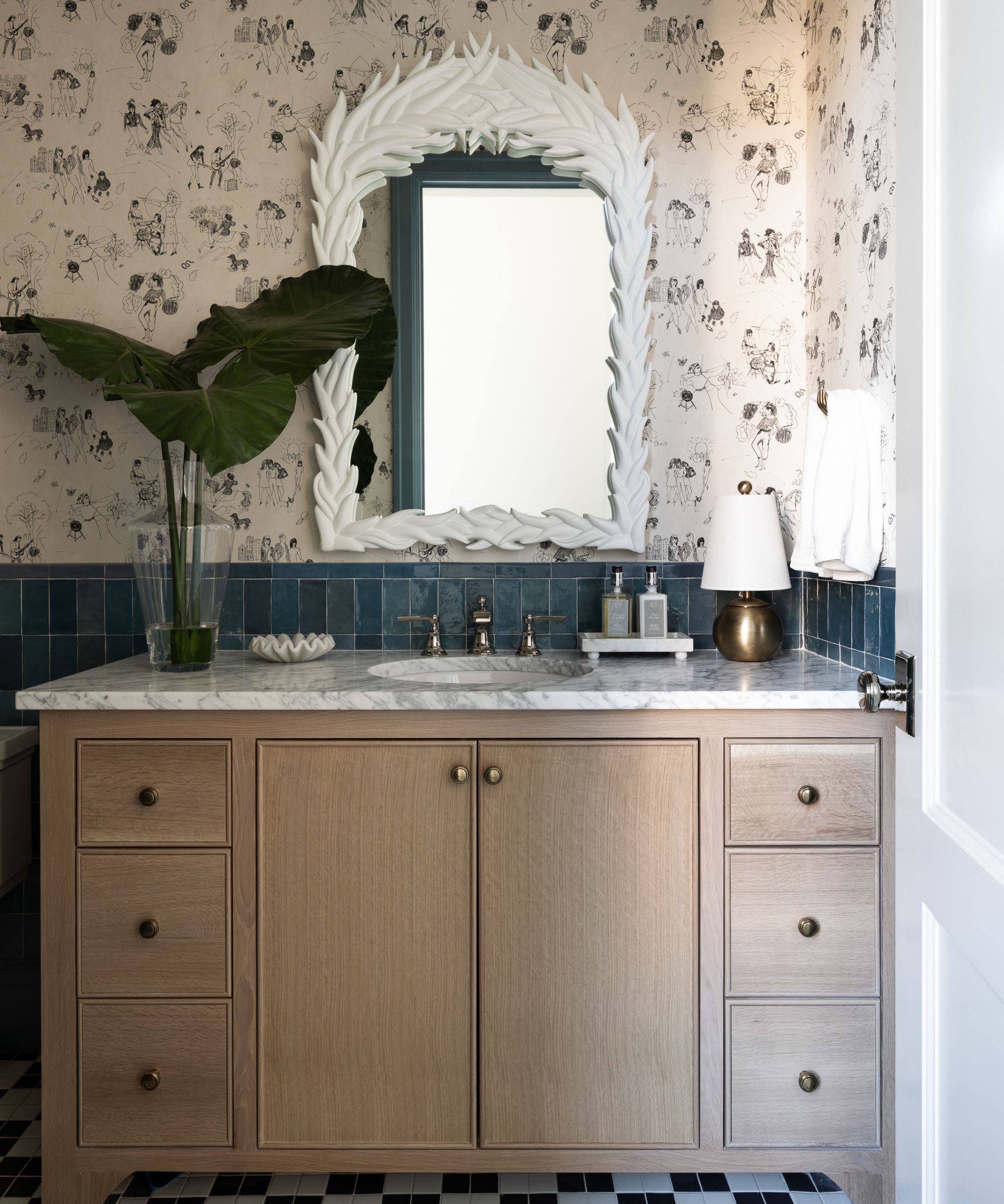 A neutral bathroom with a wooden vanity topped with a marble counter and a brass lamp