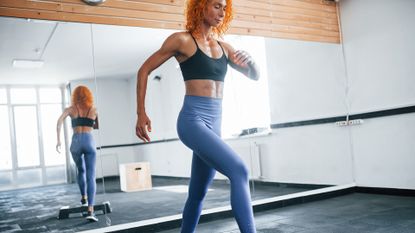 Exercise for legs. Sporty redhead girl have fitness day in gym at daytime. Muscular body type.