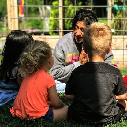 A woman smiles at a circle of children