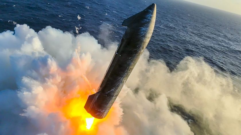 a black rocket with wing-like canards fires its engines just above the ocean, creating a spray of water vapor
