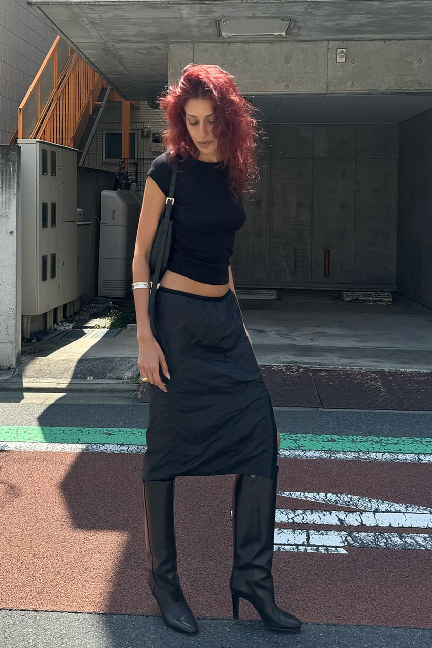 a woman wearing a black t-shirt, black low-rise skirt, and black boots