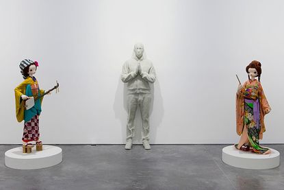 A life-sized cast of Pharrell Williams with his hand put together in a praying motion is flanked on both sides by two Kokemomos.