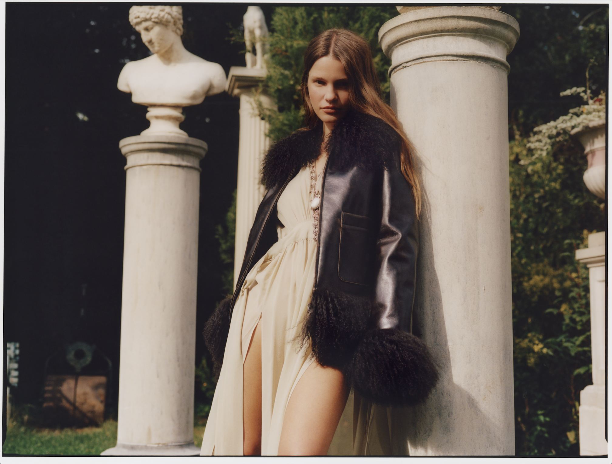 a model poses next to marble columns wearing a brown charlotte simone coat