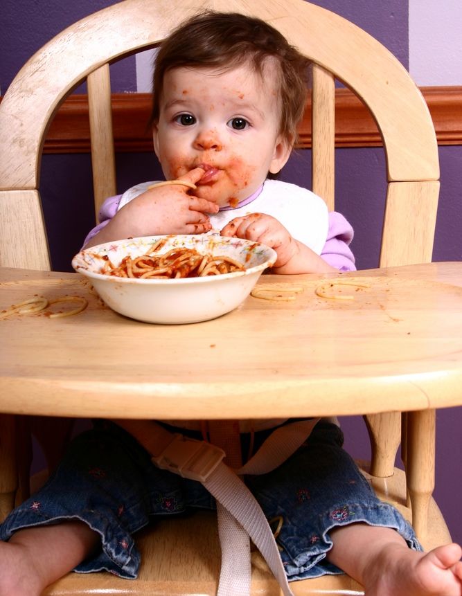 messy baby eating in high chair with spaghetti all over her face.