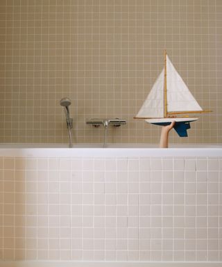 A pink tiled bathroom with a boat bath toy being held up above the rim