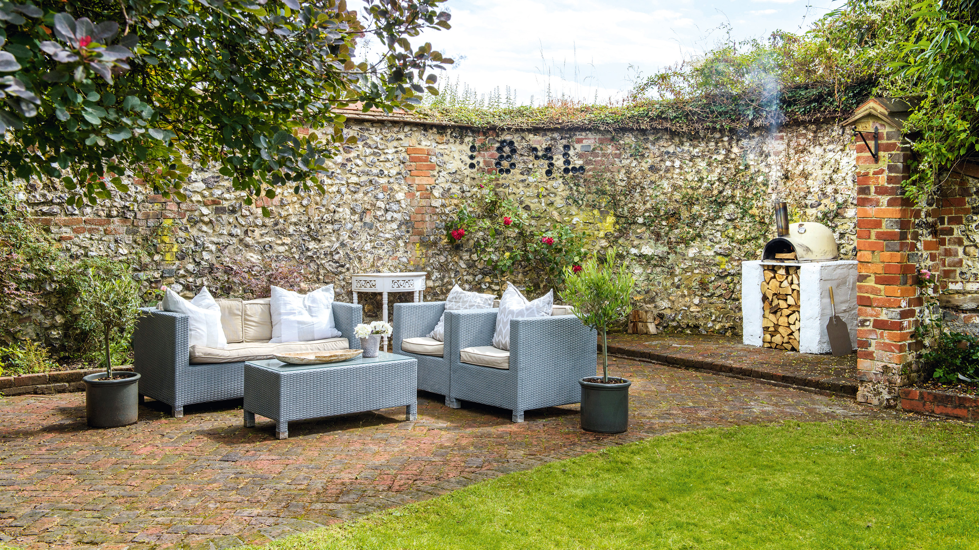 Patio with a brick and flint wall and seating area with garden chairs and sofa