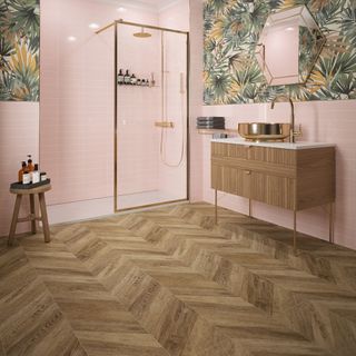 a bathroom with pink wall tiles, a green leaf patterned area on the walls with a gold trim mirror, walk-in shower and a brown chevron laminate floor