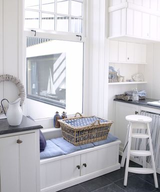 A white laundry room with blue upholstered storage bench, and white painted laundry room storage ideas and cabinetry.
