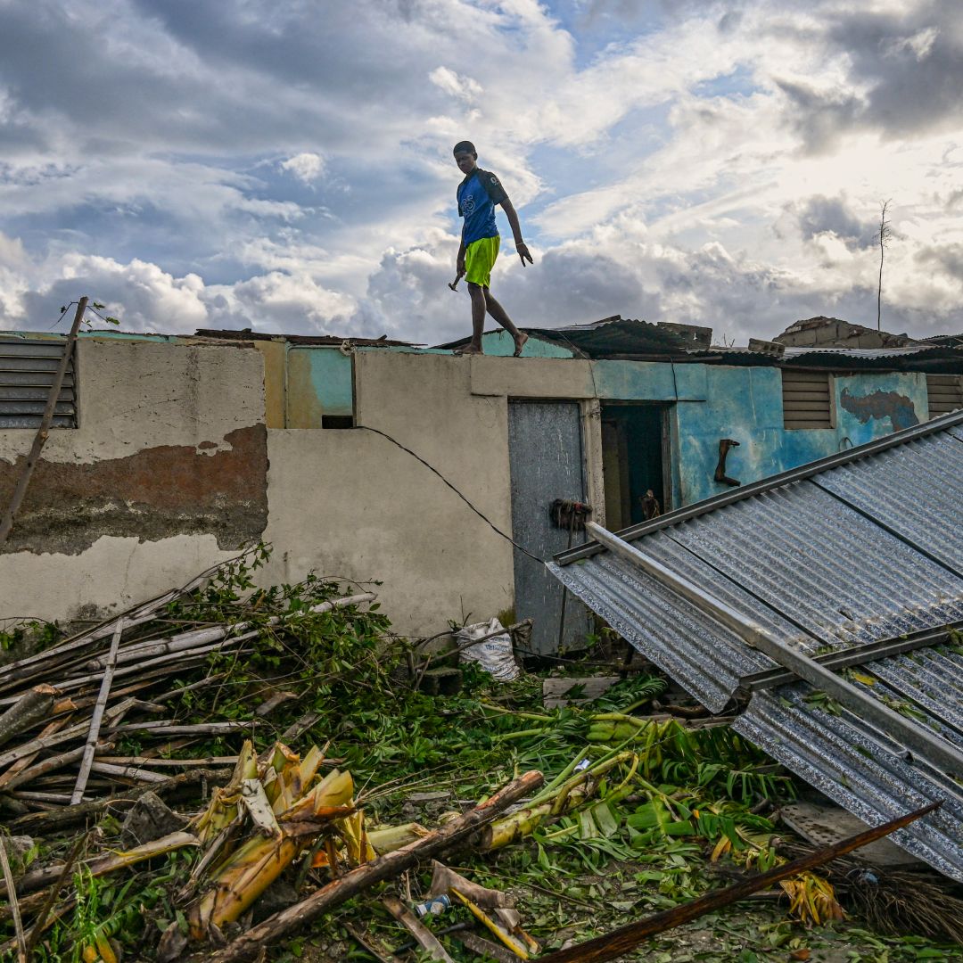 A resident of the town of El Cobre, in the province of Santiago de Cuba, walks on the roof of his damaged home after the passage of Hurricane Melissa, on October 29, 2025. Hurricane Melissa was moving towards Bermuda on Thursday after ripping a path of destruction through the Caribbean that left at least 20 people dead in Haiti, and parts of Jamaica and Cuba in ruins. 