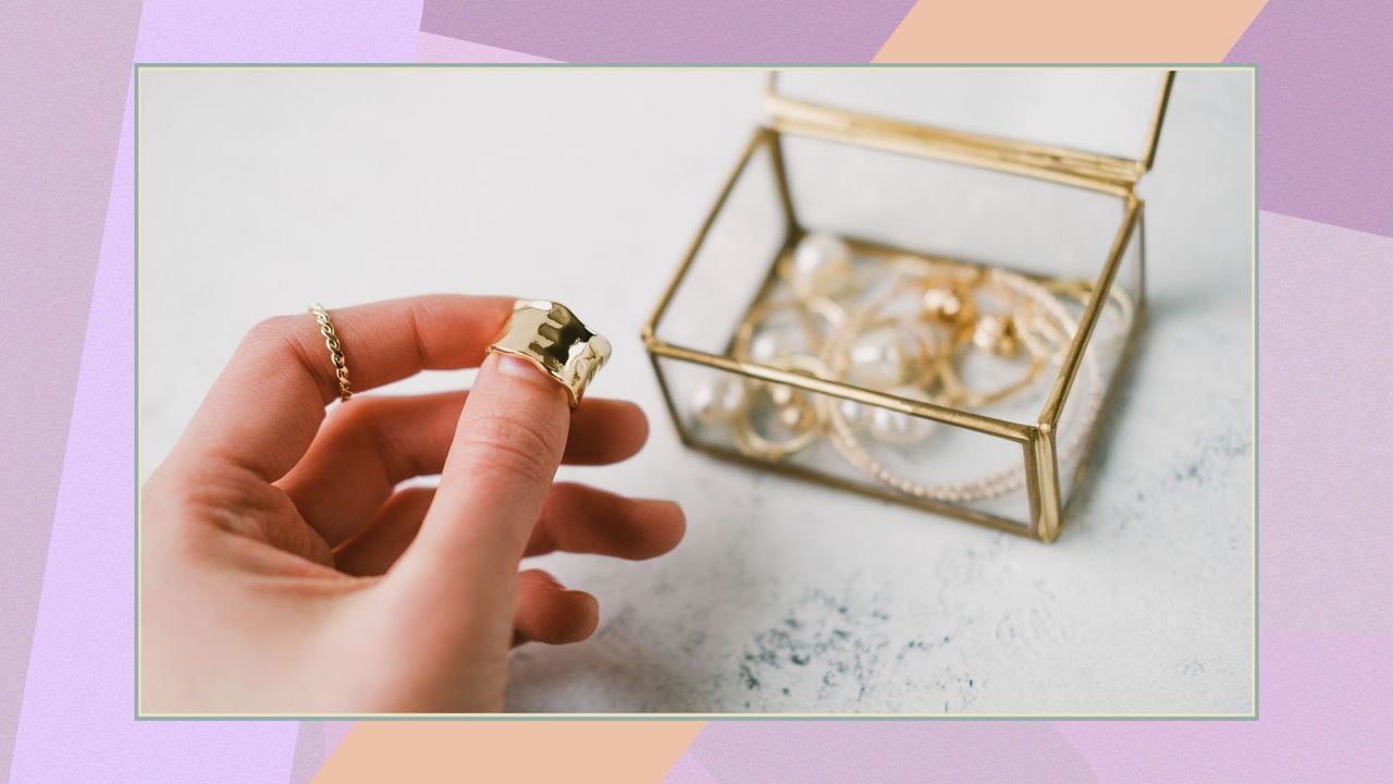 A woman&#039;s hand holds a gold ring on the background of a transparent jewelry box with accessories on a colorful background