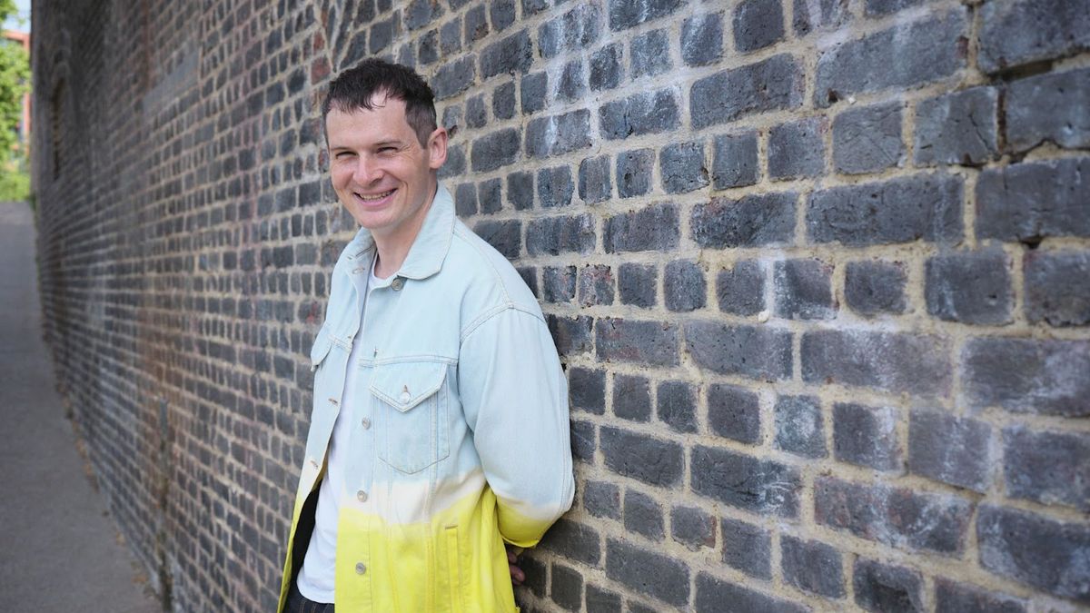 Ian Hogarth, the Foundation Model Taskforce&#039;s chair, wearing a jacket that fades from pale blue at the top to yellow at the bottom, standing against a brick wall.