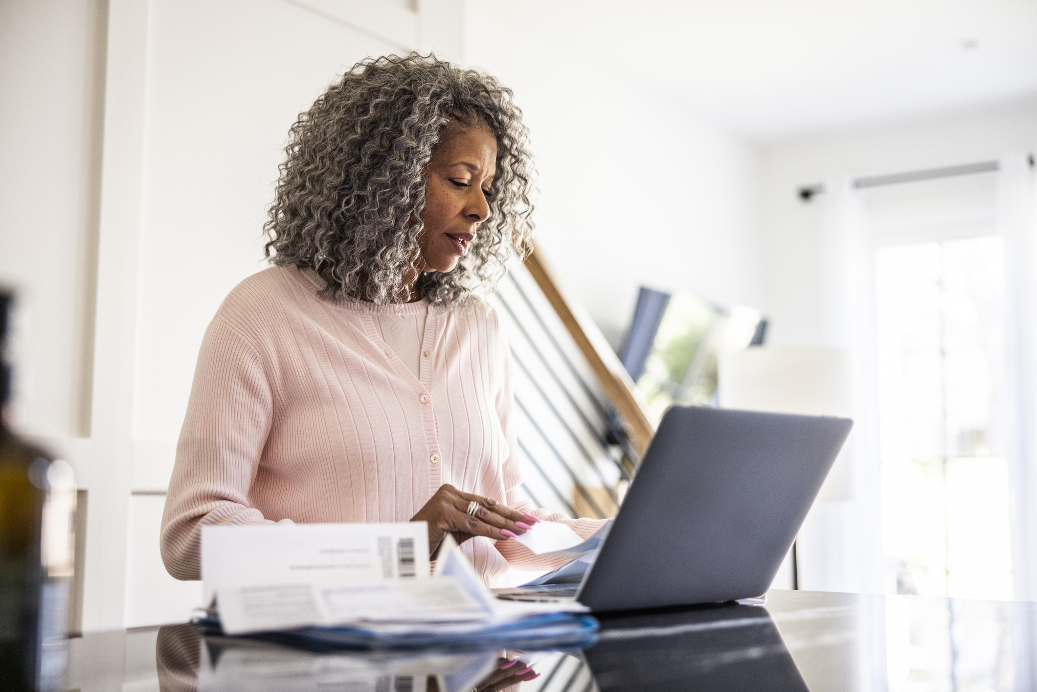 Person who has reached state pension age looks at finances as she sits in front of laptop at kitchen table.