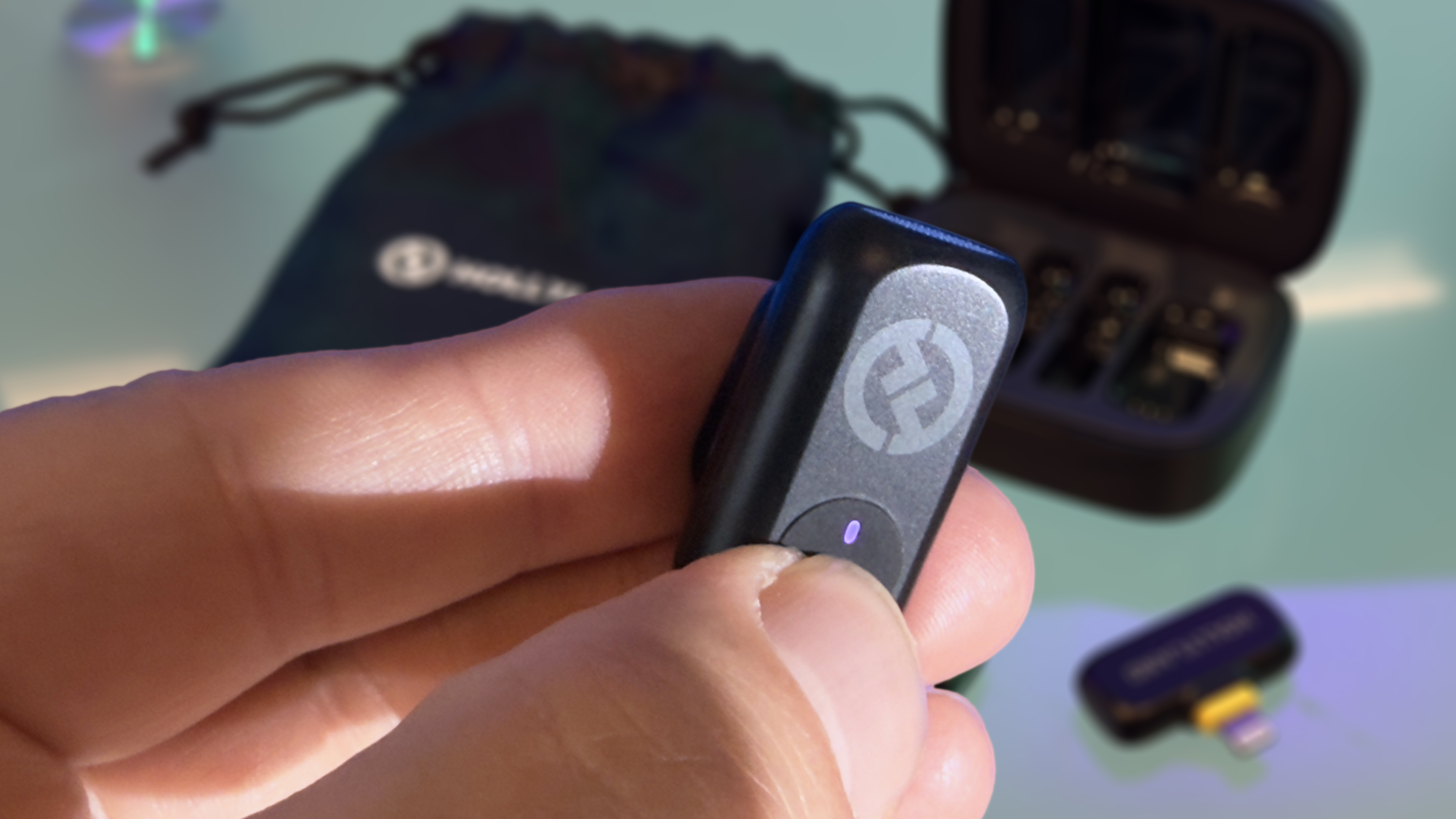 Close-up of a finger pressing the circular button on front of the tiny transmitter mic