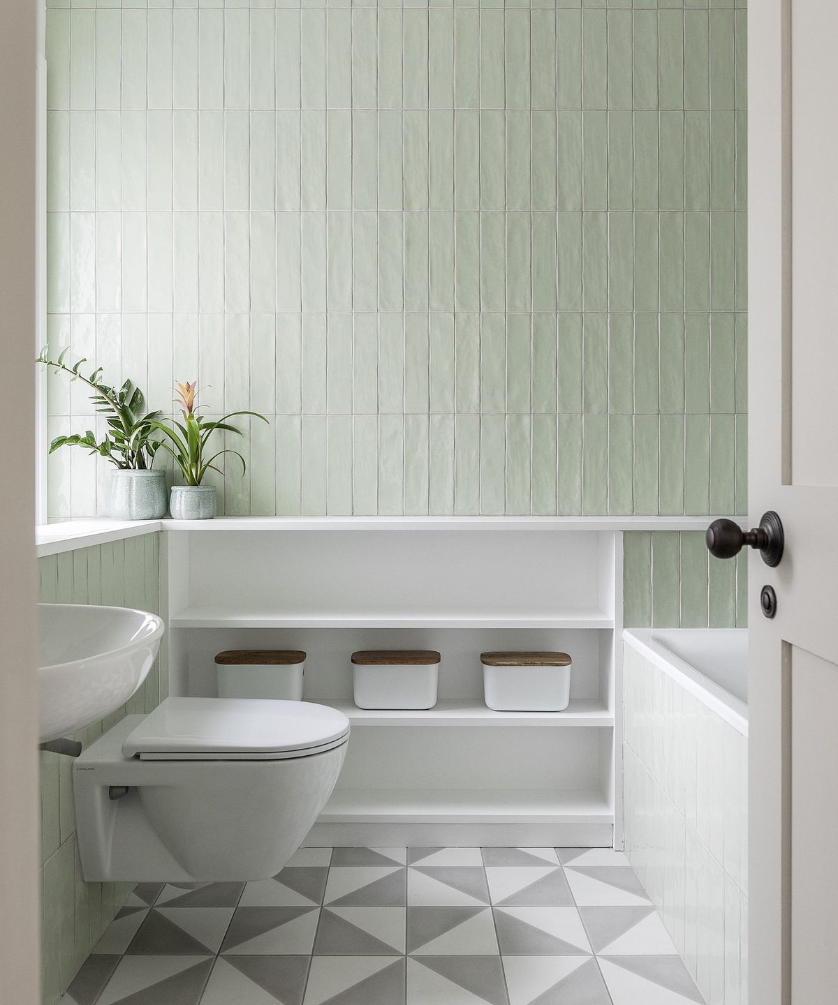 A bathroom with pale green tiles on the wall and white and grey patterned floor tiles