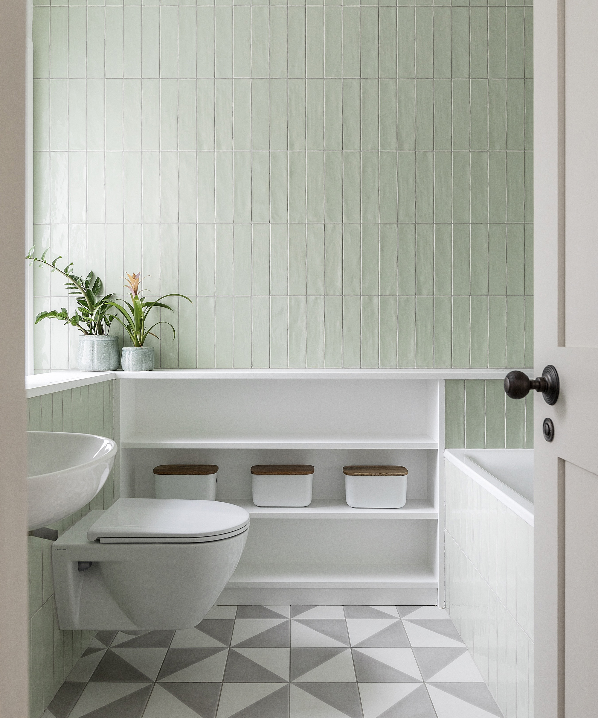 A bathroom with pale green tiles on the wall and white and grey patterned floor tiles