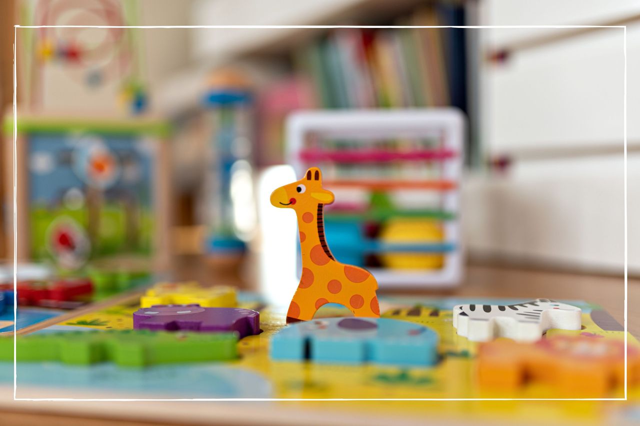 Close up of giraffe toy figure, with other animal figures lying down on a mat on the floor in a nursery environment