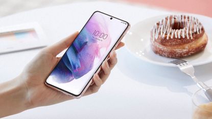 Samsung Galaxy S22 being held by a woman next to a plate with a donut on it