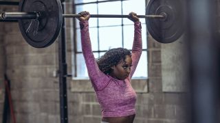 Woman performs overhead press shoulder exercise with a barbell