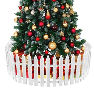 An artificial christmas tree with red and gold baubles with presents underneath. There is a white picket fence all around the base