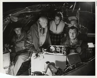 A group of bundled people huddle around a control station