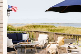 beach house deck with wooden outside furniture sea view and blue parasol with stars and stripes flag visible
